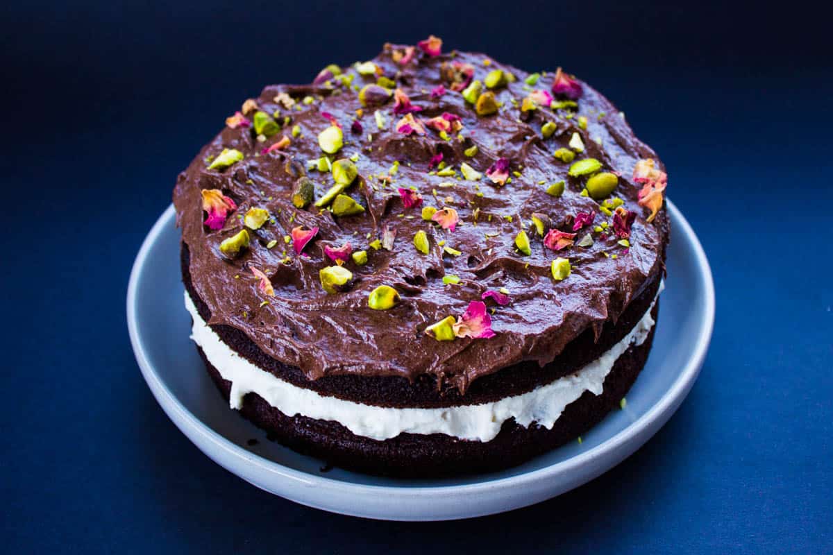 Vegan gluten free chocolate cake with coconut cream chocolate frosting and decorated with pistachios and rose petals.