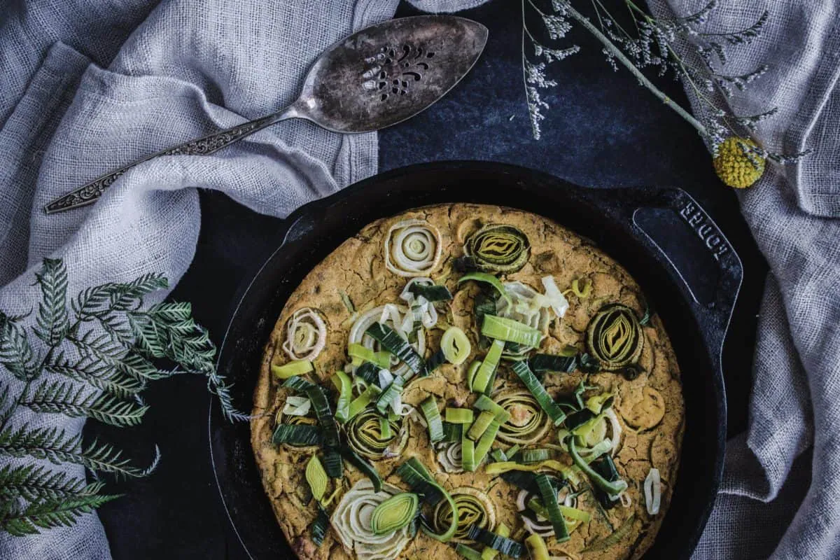 Overhead shot of Vegan Leek & Onion Frittata in cast iron skillet. Frittata is decorated with leek and onion discs.
