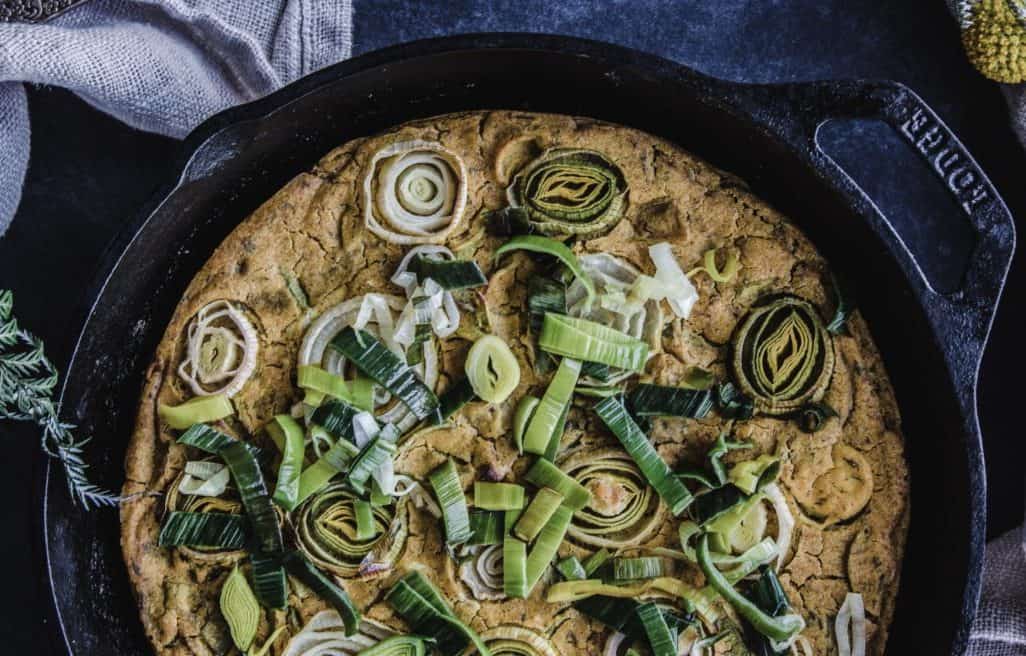 Close up overhead shot of Vegan Frittata with Leek & Onion in cast iron skillet. Frittata is decorated with leek and onion discs.