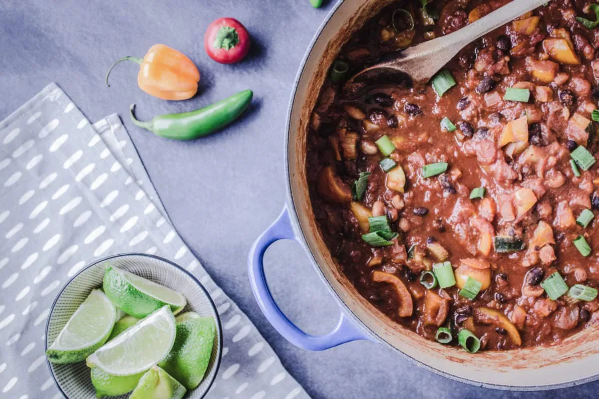 A pot of Warming Bean Chili, with other meal prep ingredients nearby such as lime and chilis.