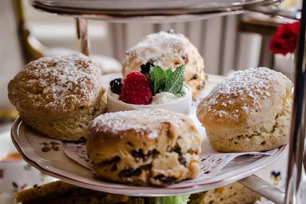 Image shows a close-up of the scones from Egerton House's Vegan Afternoon Tea in London. The middle tier of a cake stand is shown, featuring four scones surrounding a dish of coconut cream and berries.
