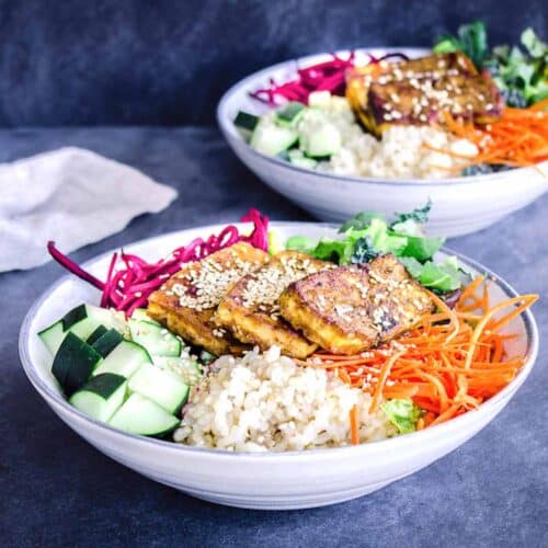 Close up image of vegan buddha bowls containing tofu, brown rice, carrots, beets, greens and cucumber, next to linen napkin.