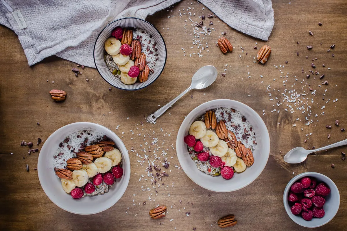 Overhead shot of bowls of Chocolatey Pecan Chia Cereal, decorated with fruit, coconut and nuts.