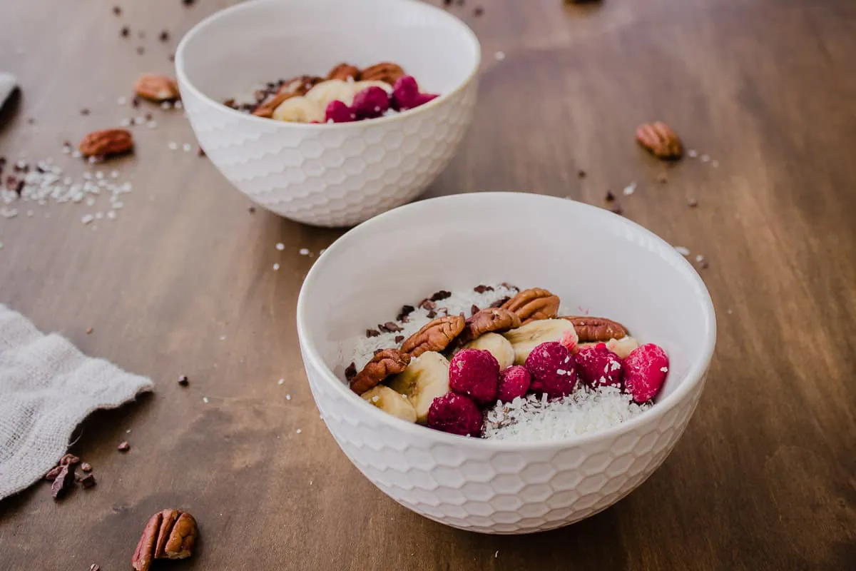Two bowls of Chocolatey Pecan Chia Cereal , decorated with fruit, coconut and nuts.