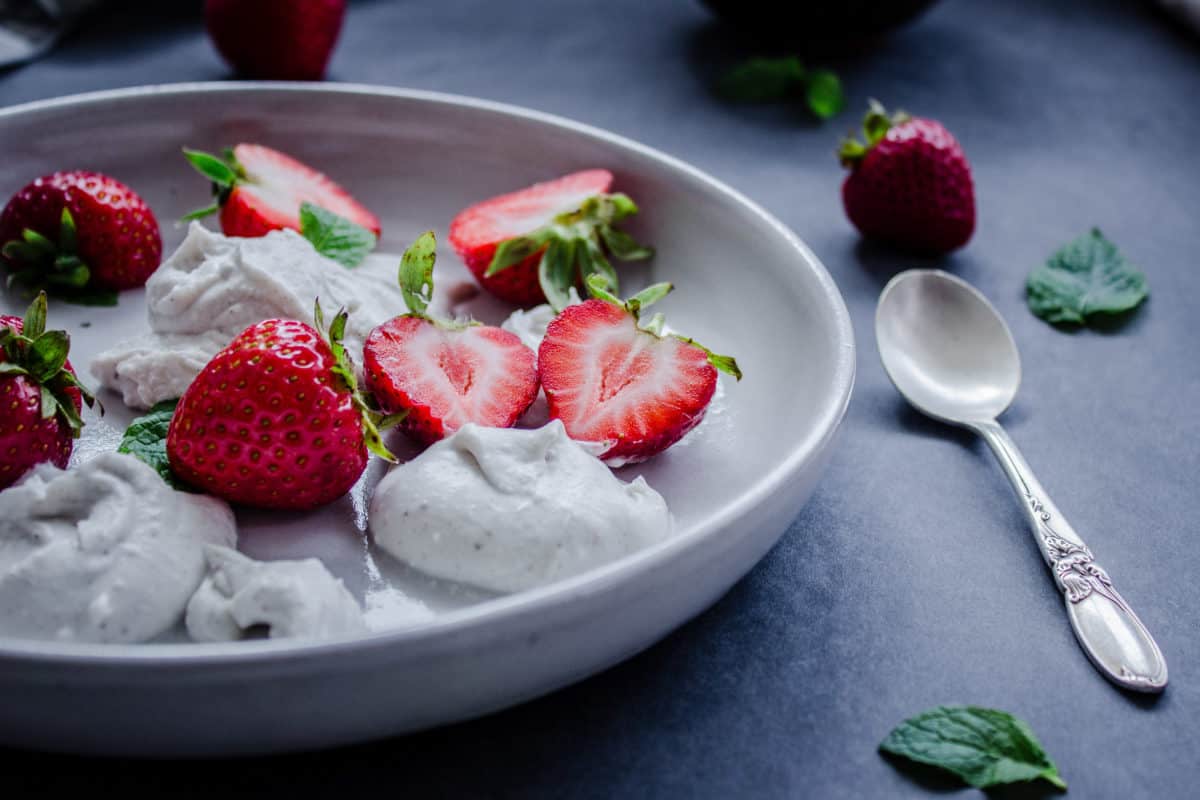 Plate of Easy Vegan Strawberries & Cream, surrounded by a spoon, mint leaves & strawberries.