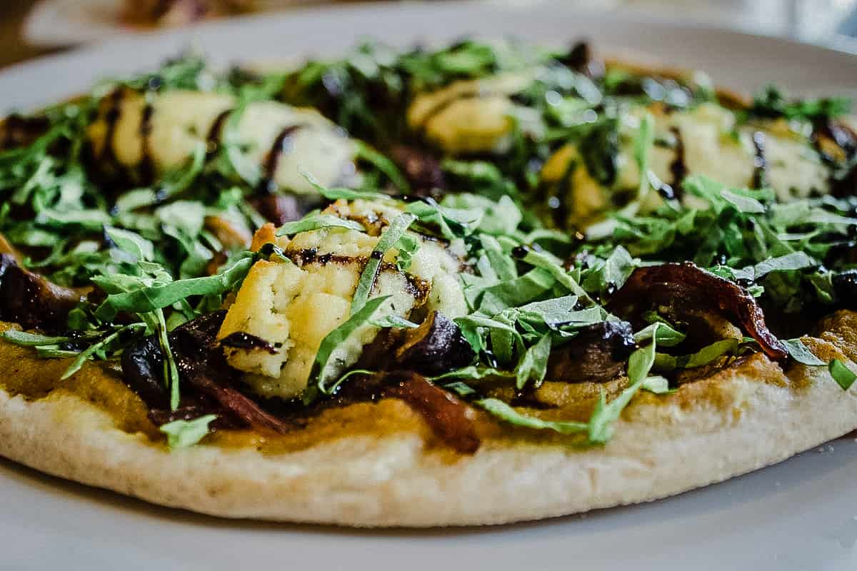Close-up image of pizza topped with vegan cheese, greens and mushrooms from The Arbor Restaurant - the best vegan restaurants in Vancouver.