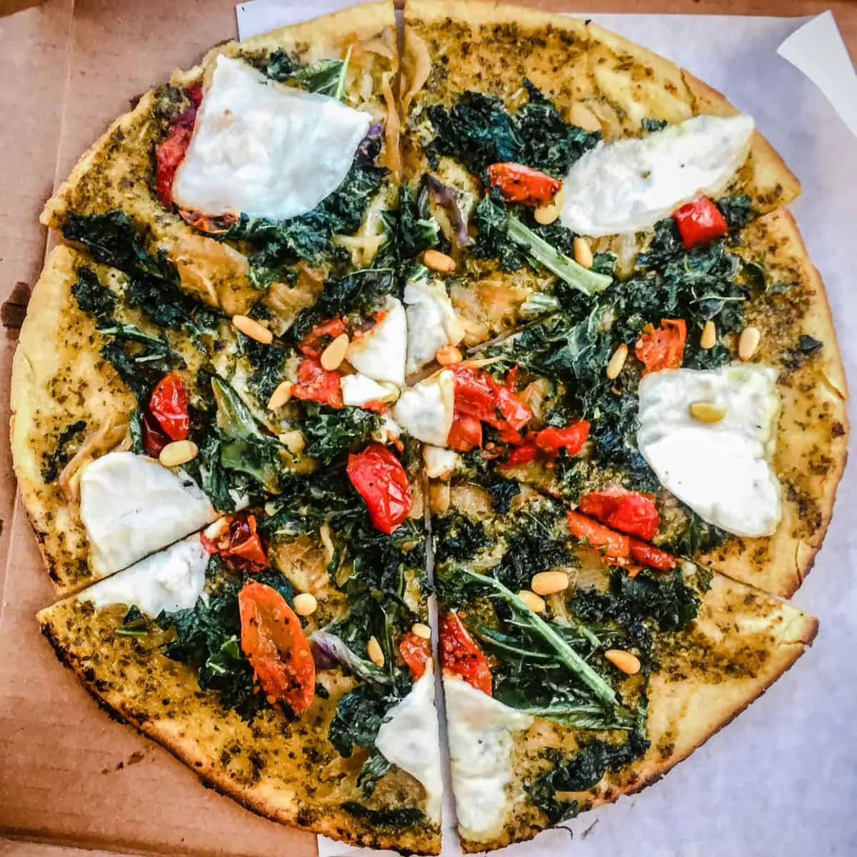 Overhead shot of pizza topped with vegan cheese, tomatoes, kale and pine nuts from Virtuous Pie Restaurant in Vancouver.