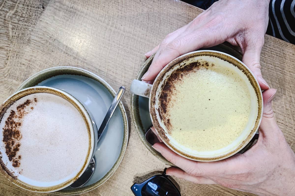 Image of My Favourite Vegan Restaurants in London - overhead shot of mugs of chai and turmeric lattes with womans hands at Deliciously Ella Deli