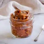 How to Make Date Paste - image of a glass jar of date paste surrounded by a spoon and beige linen napkin on a marble surface.