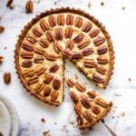 Easy vegan pecan pie decorated with concentric circles of pecans, with a slice being taken out of it.