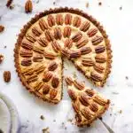 Easy vegan pecan pie decorated with concentric circles of pecans, with a slice being taken out of it.