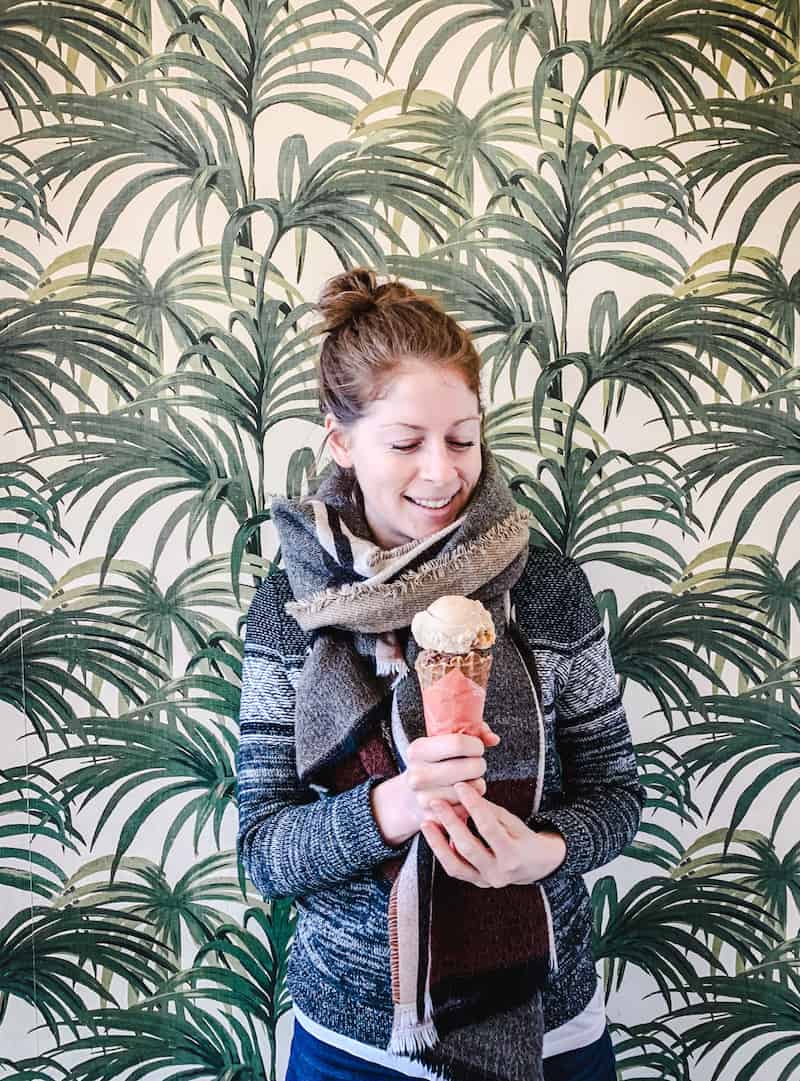My Favourite Vegan restaurants in Seattle - Vancouver with Love. Image of a woman holding Frankie & Jo's ice cream cone against pam tree wallpaper.