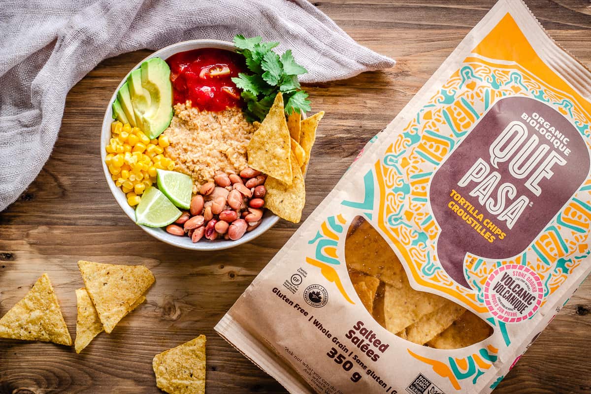 Overhead image of Savoury Vegan Oatmeal in large bowl on wooden background next to a bag of Que Pasa Tortilla Chips.