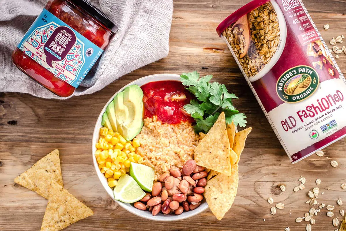 Overhead image of Savoury Vegan Oatmeal in large bowl on wooden background next to a jar of Que Pasa Mexicana Salsa and Nature's Path Old Fashioned Oats.