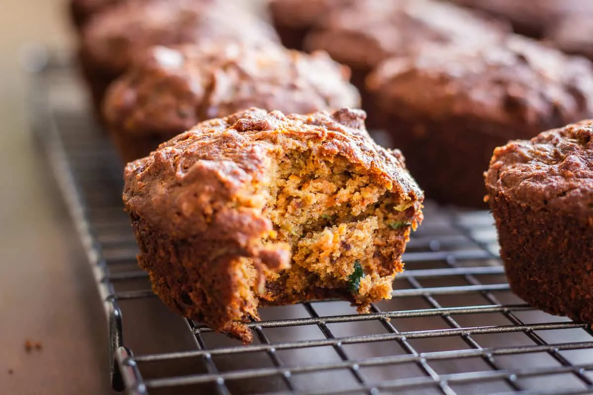 Close up image of Carrot Cake Muffins. Image shows a row of muffins on a wire cooling rack. One muffin has a bite taken out of it.