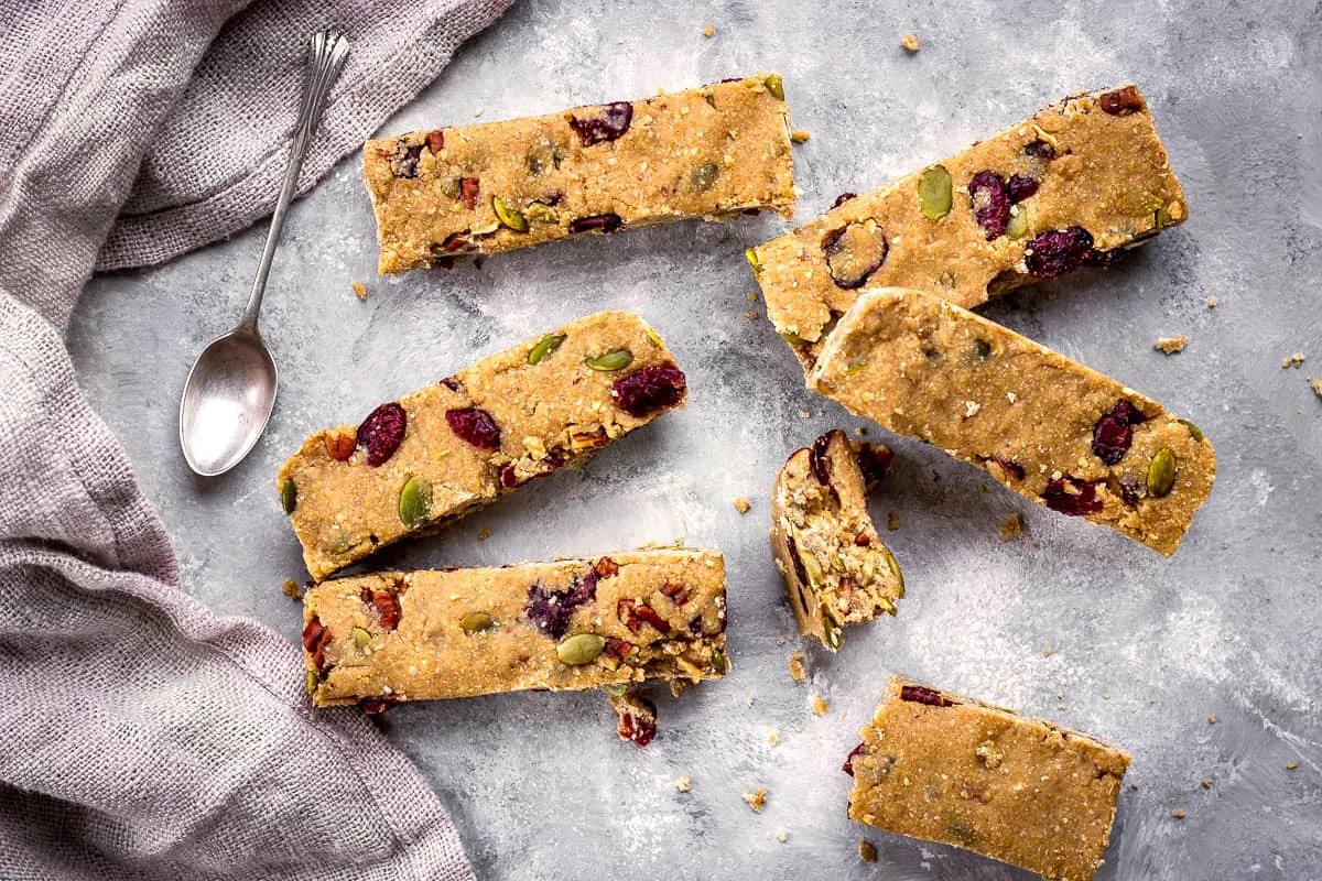 Image of vegan granola bars with cranberries, nuts and pumpkin seeds on a grey mottled background with a silver spoon and linen napkin.