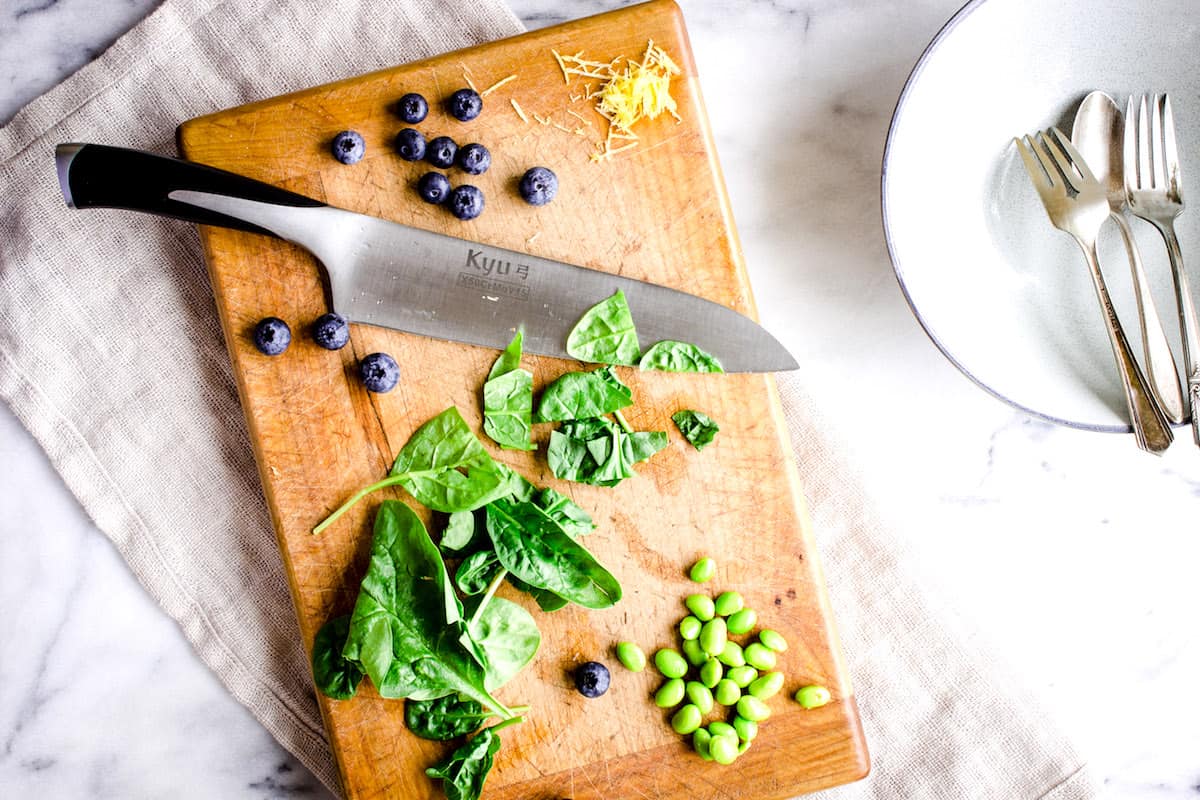 How to Vegan Meal Prep - image shows a chopping board covered in spinach leaves, edamame, and blueberries ready for use.