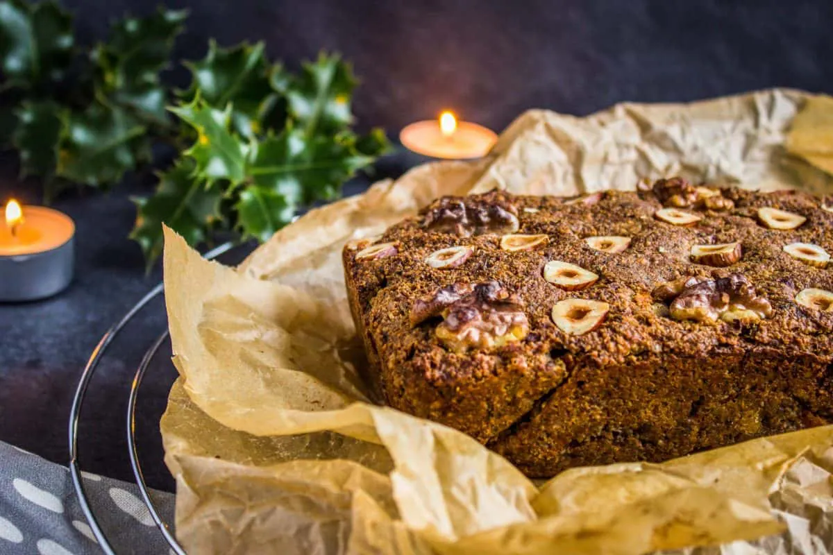 Closeup view of Classic Vegan Nut Roast. Nut roast is on a wire cooling rack, surrounded by a grey napkin, candles and holly/pine branches.