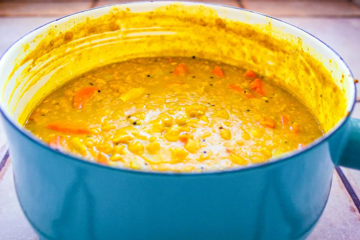 Close up image of Red Lentil Dhal in blue enamel saucepan on tiled surface. The dhal is a deep golden yellow with carrots in.