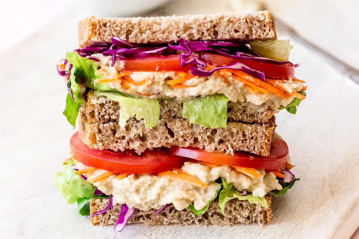 Close up image of White Bean & Artichoke Vegan Sandwich on a white chopping board.