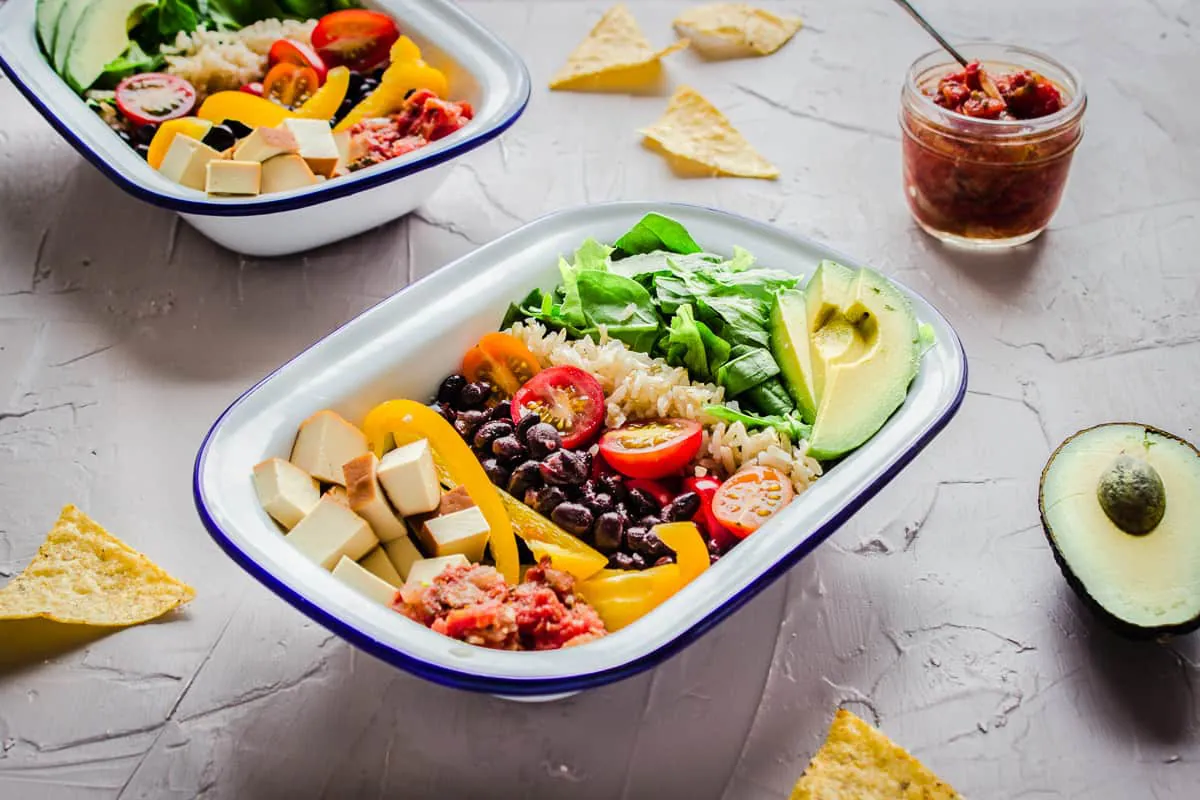 Healthy burrito bowls made with rice, tofu, black beans, colourful peppers and tomatoes.