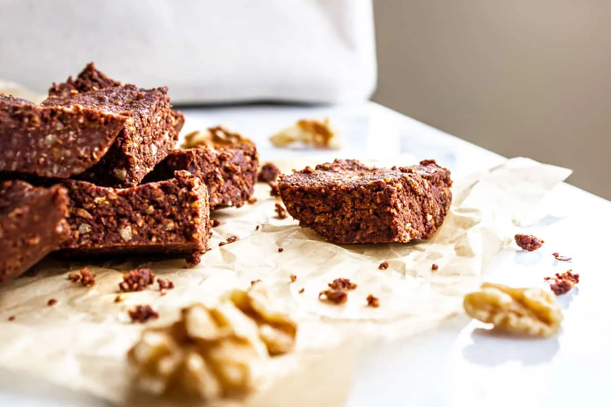 Image of brownies on the side of a white marble table. The brownies are sitting on baking parchment and walnuts are scattered around them.