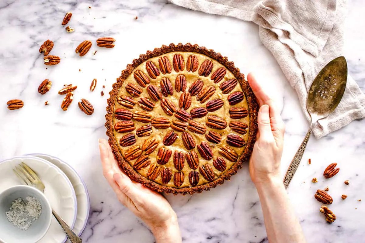 A woman's hands hold a pecan pie decorated with concentric circles of pecans.