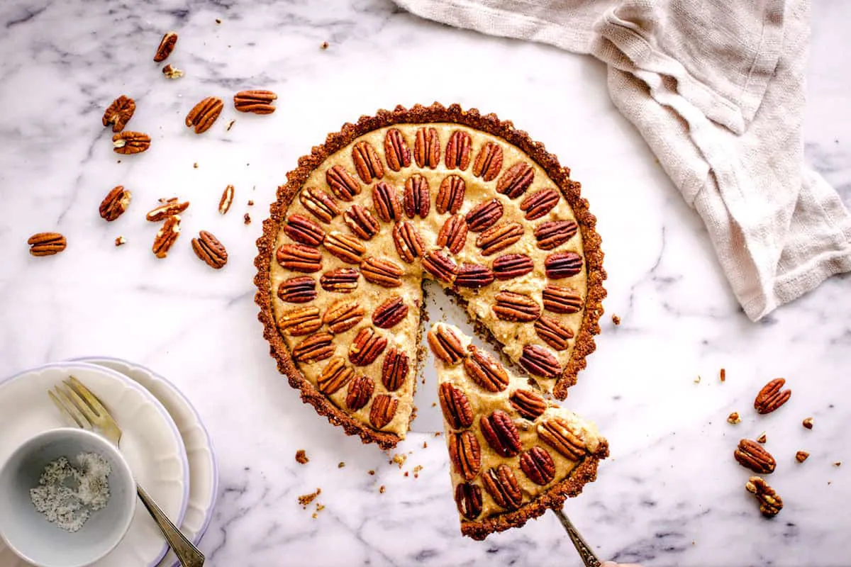 Pecan pie decorated with concentric circles of pecans, with a slice being taken out of it.