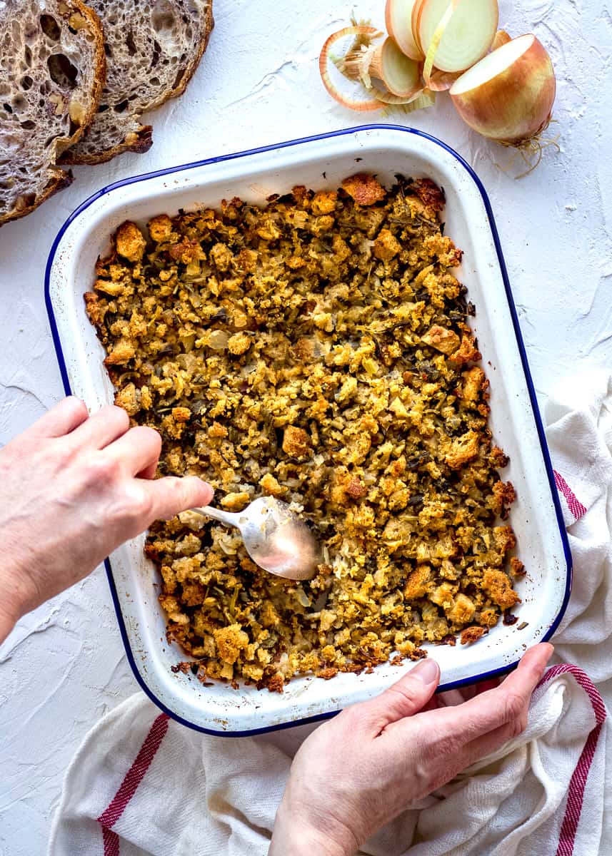 A tray of vegan gluten free stuffing with a woman's hand spooning some out.