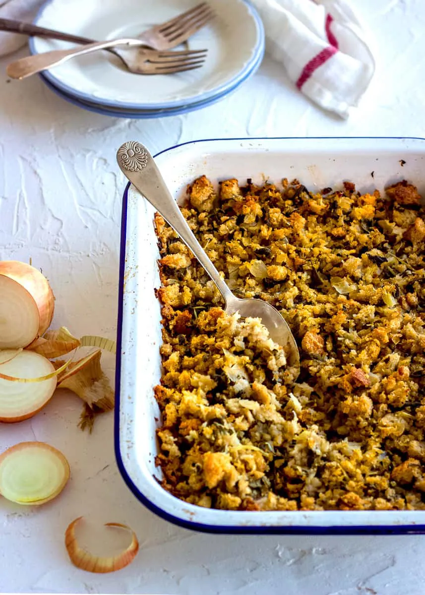 Vegan gluten free stuffing in an ovenproof dish with onion slices nearby.