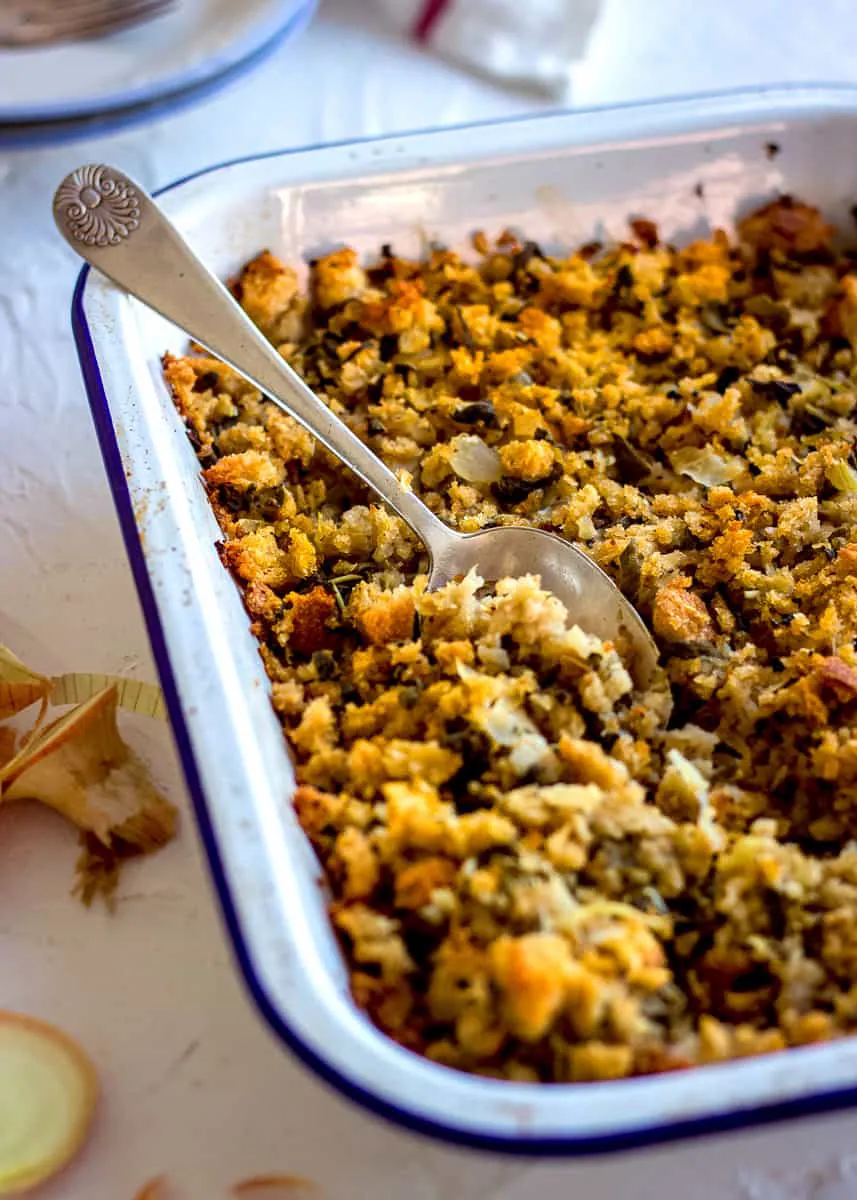Vegan gluten free stuffing in an ovenproof dish with a spoon.