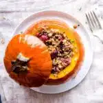 Overhead shot of Stuffed Pumpkin, showing a pumpkin with its lid off, stuffed with cranberries, rice and nuts on a white plate.