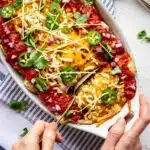 A pair of hands spoons out a Black Bean Vegan Enchilada from its dish.