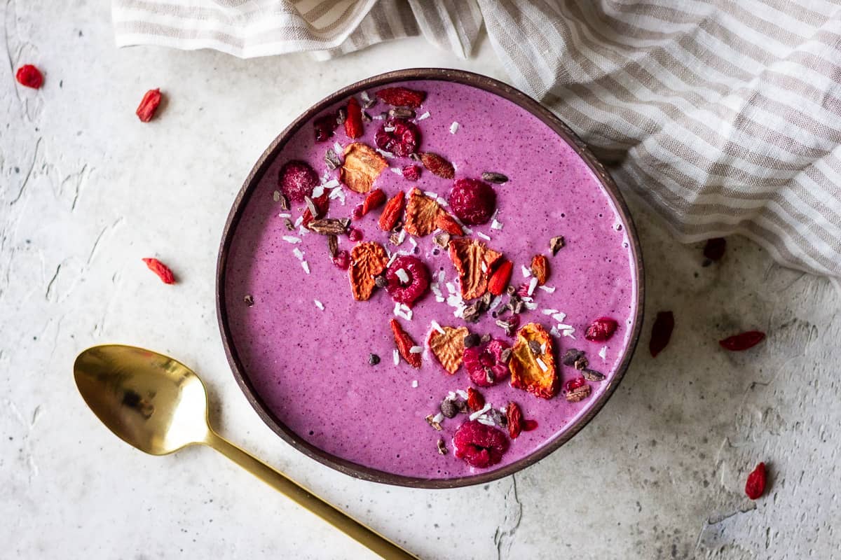 Purple berry smoothie bowl decorated with raspberries, freeze-dried strawberries, coconut and cacao 
