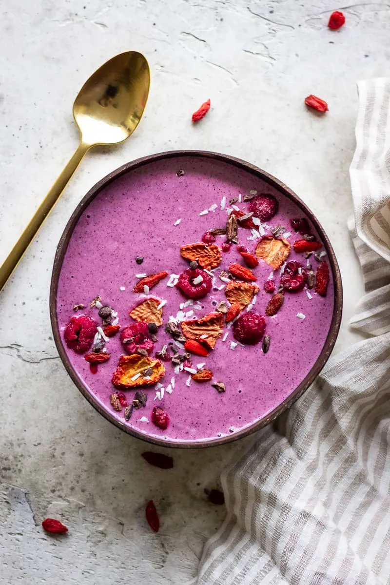 A bright pink smoothie bowl decorated with berries and a gold spoon.