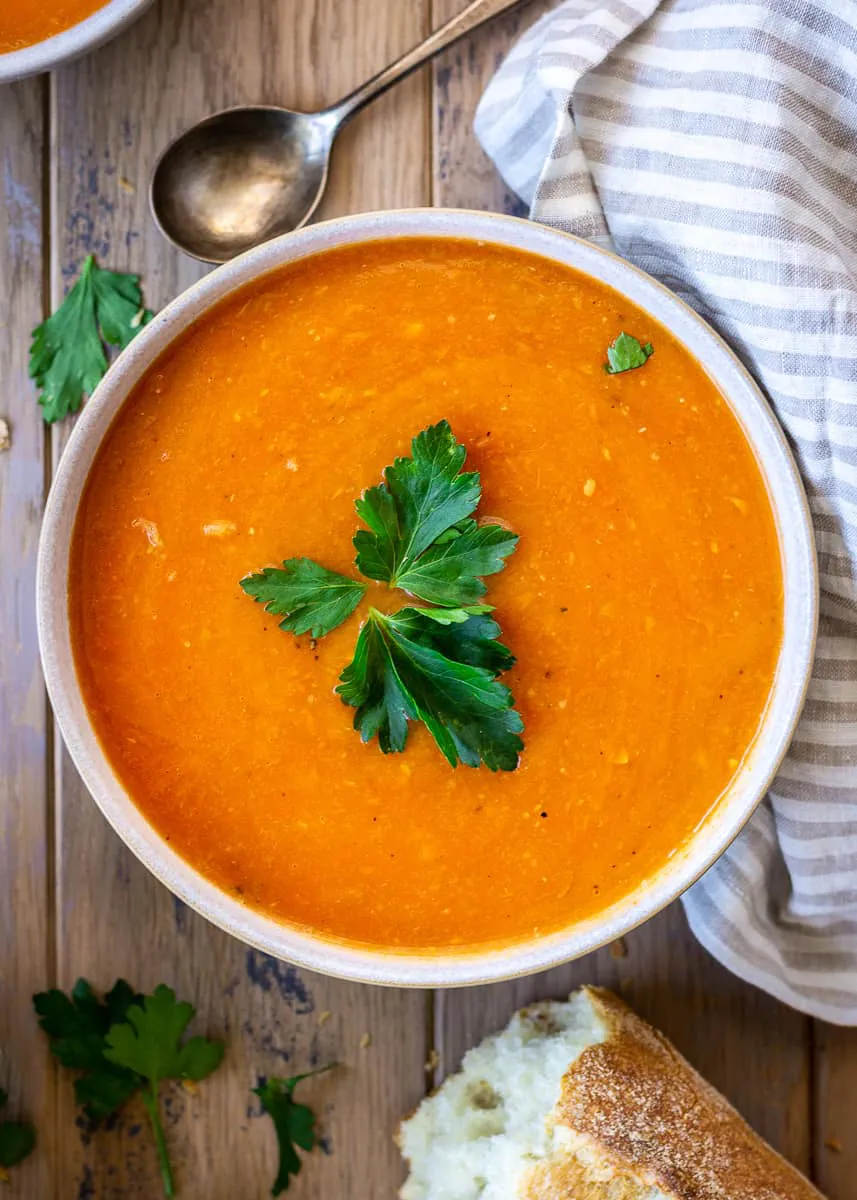 Bright orange soup decorated with a leaf of parsley.