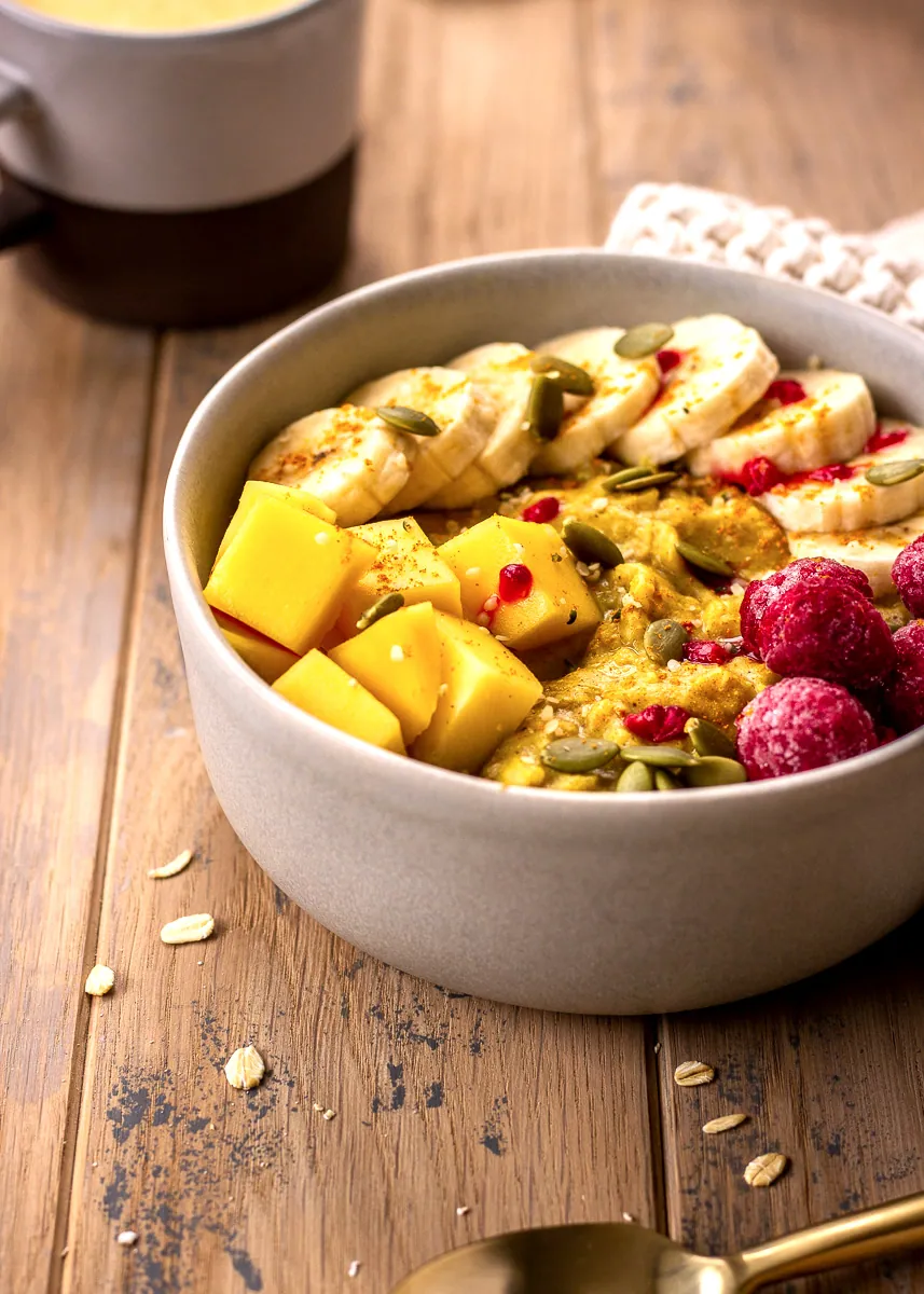 Golden Turmeric Oatmeal in a bowl decorated with mango, raspberries and banana slices