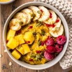 Golden Turmeric Oatmeal in a bowl decorated with mango, raspberries and banana slices.