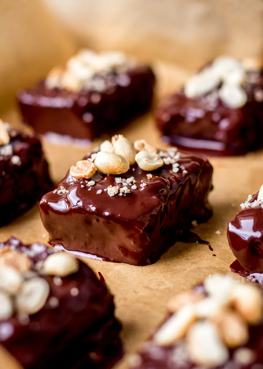 Vegan snickers bars dipped in melted chocolate on parchment paper.