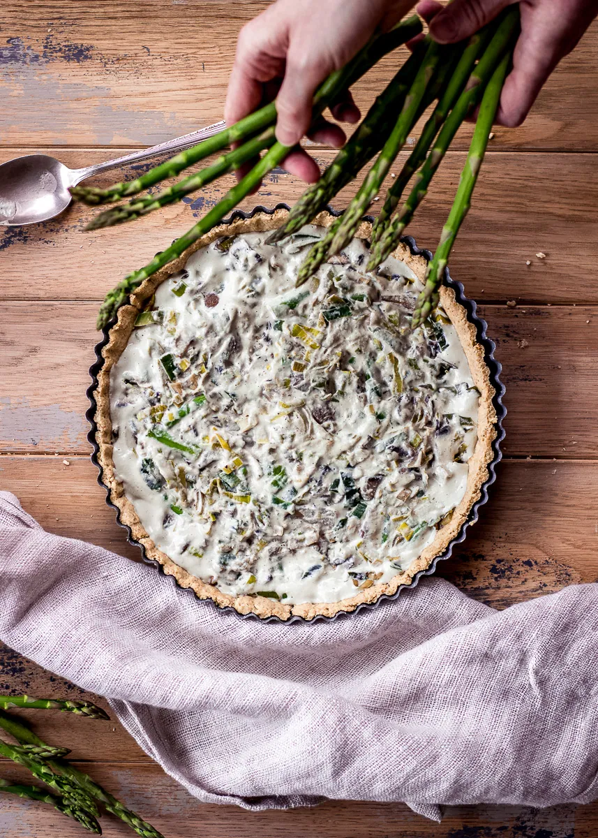 A woman's hands decorating a quiche with asparagus spears.