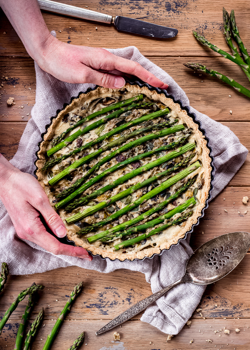 A woman's hands holding a vegan quiche decorated with asparagus tips.