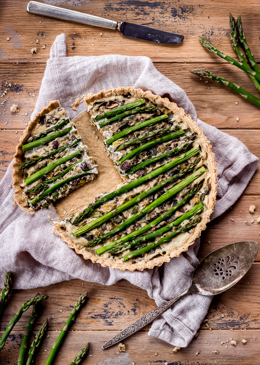 A quiche with a slice taken out decorated with asparagus spears.