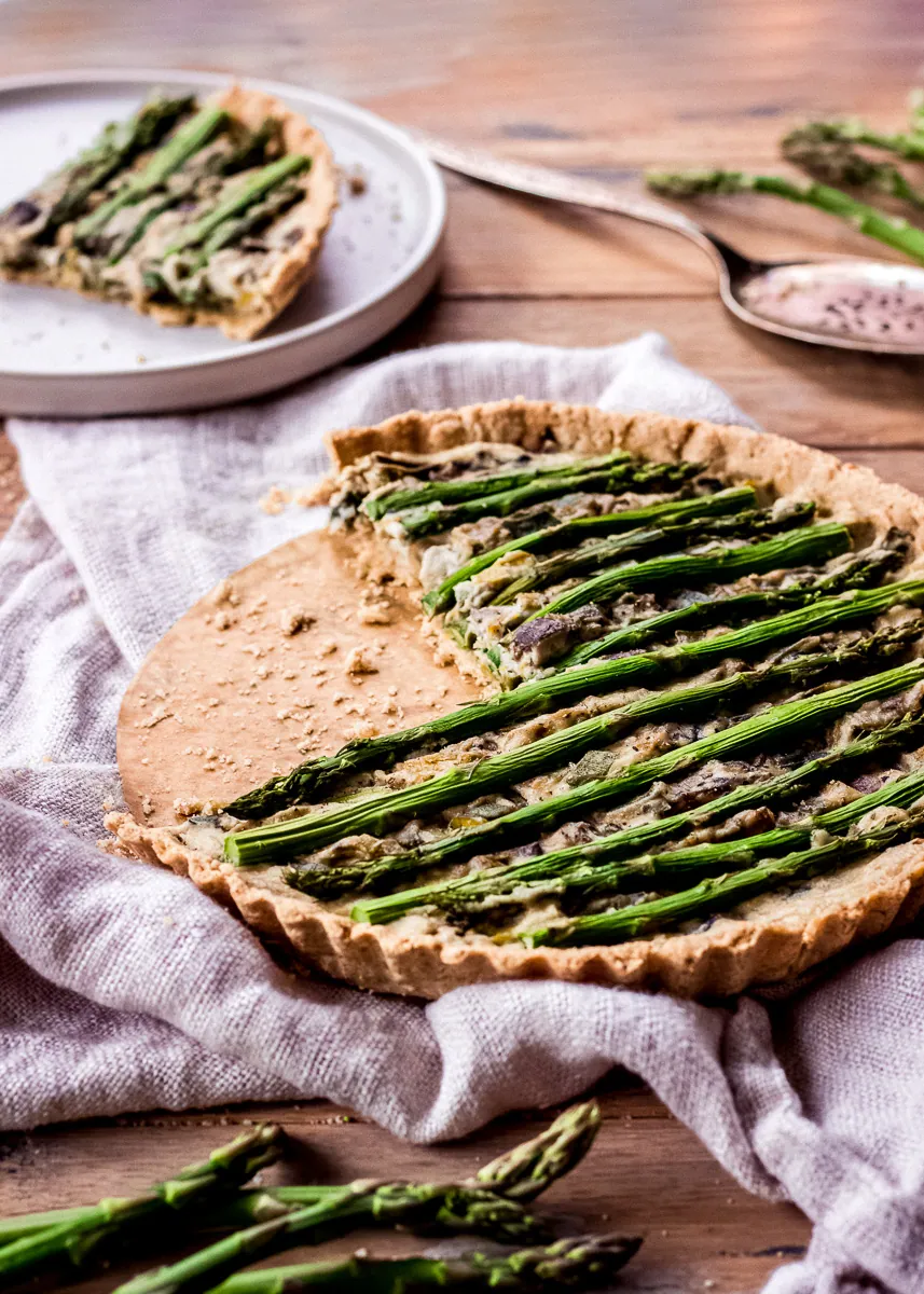 Asparagus & Leek Vegan Quiche on a wooden table with asparagus spears decorating it.