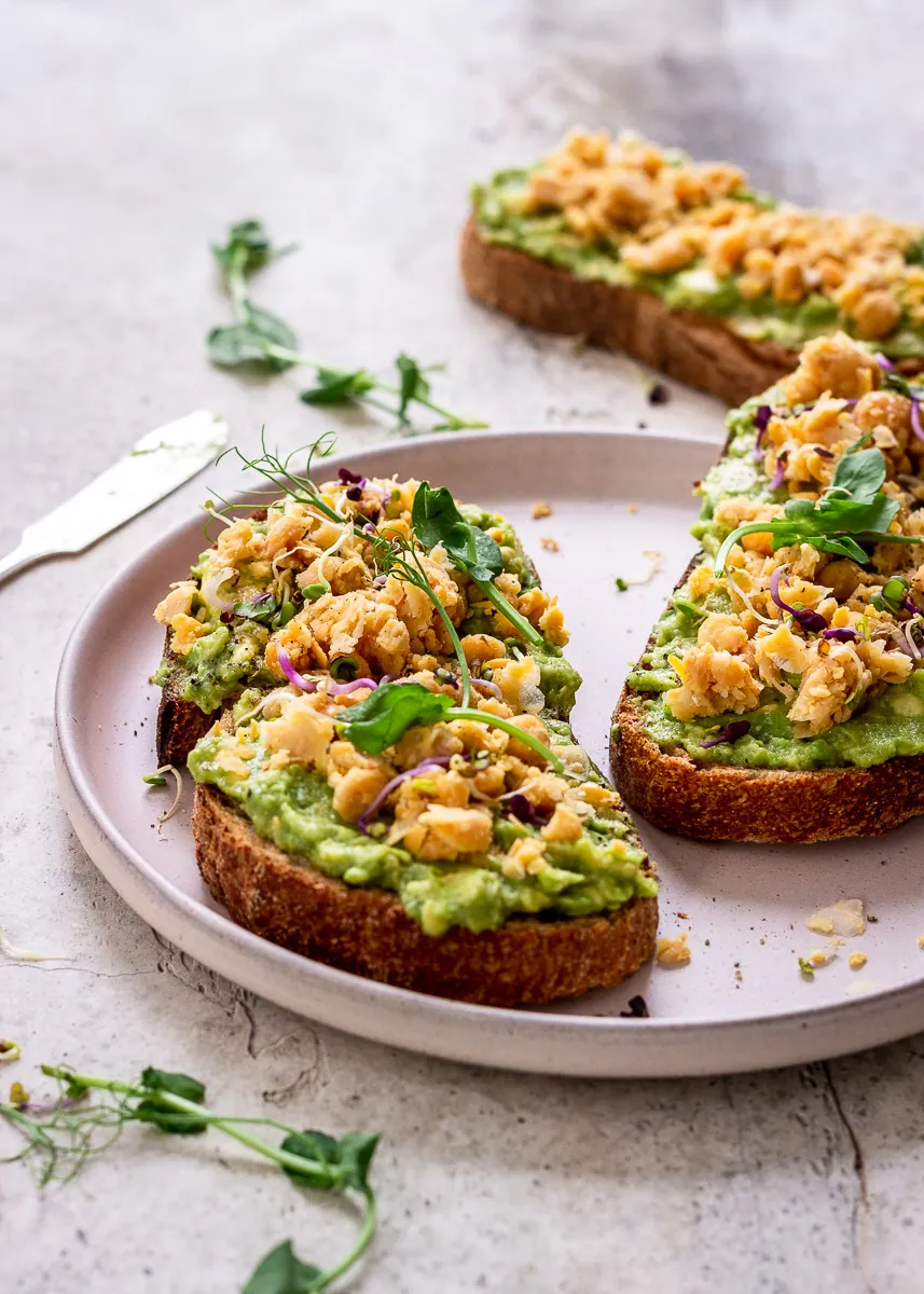 Toast with smashed avocado, chickpeas and microgreens on a plate.