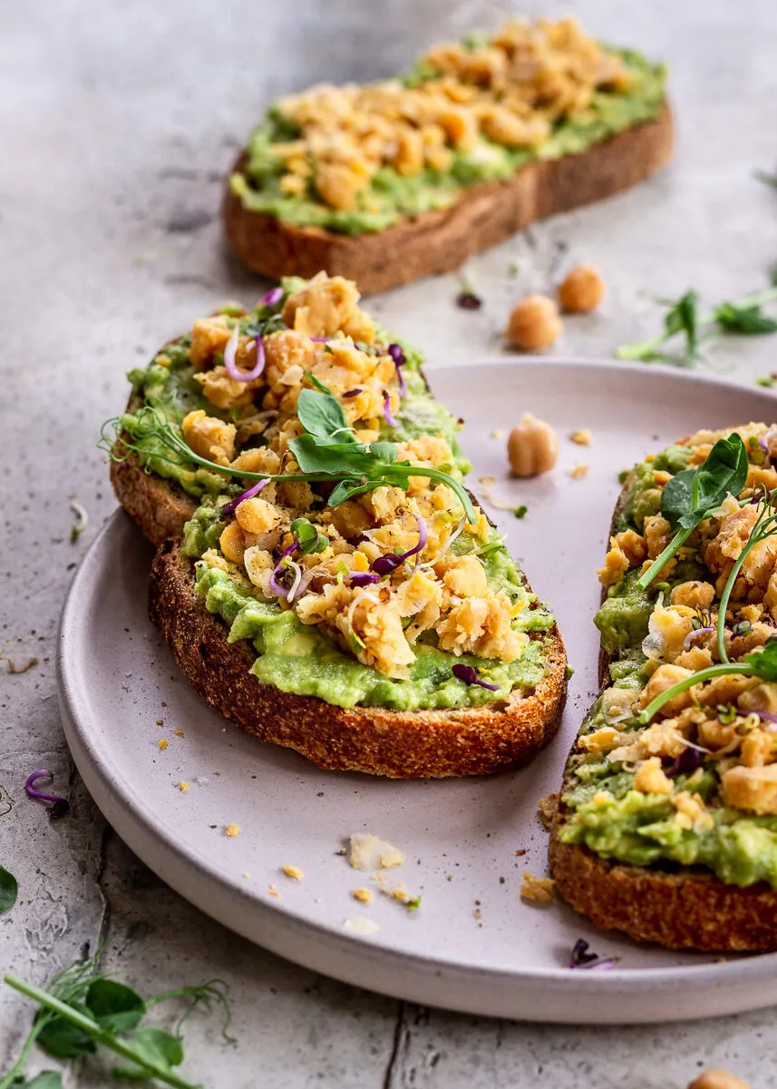 Toast with avocado and smashed chickpeas on a pink plate.