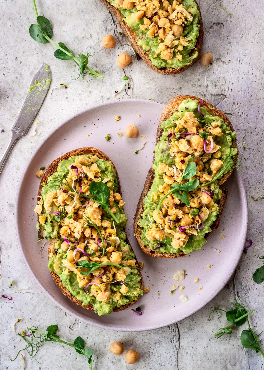 Protein-Packed Avocado Toast with chickpeas and microgreens on a pink plate.