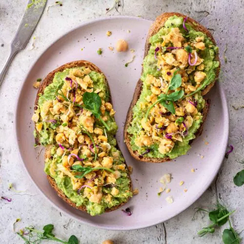 Protein-Packed Avocado Toast with chickpeas and microgreens on a pink plate.