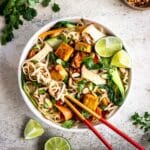 Almond Butter Tofu Noodles in a bowl with chopsticks and garnished with lime and cilantro.