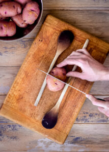 Potato being sliced, with a wooden spoon either side of it to stop slices going all the way through.