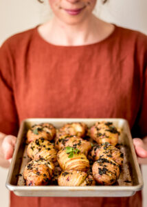 Woman holding a tray of hasselback potatoes.